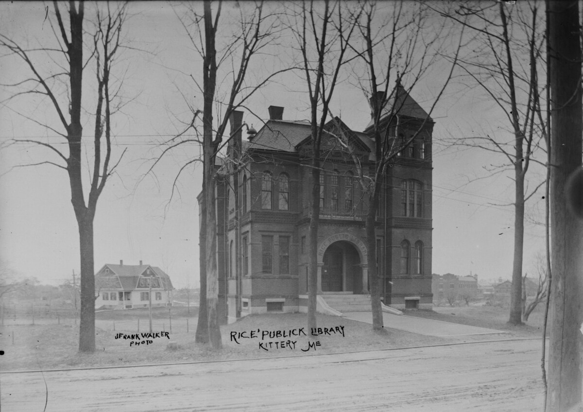 Black-and-white photo of the Rice Public Library in Kittery, Maine, showing a large brick building with arched entrance, pointed towers, and leafless trees in front. Handwritten notes and a house are visible in the background.