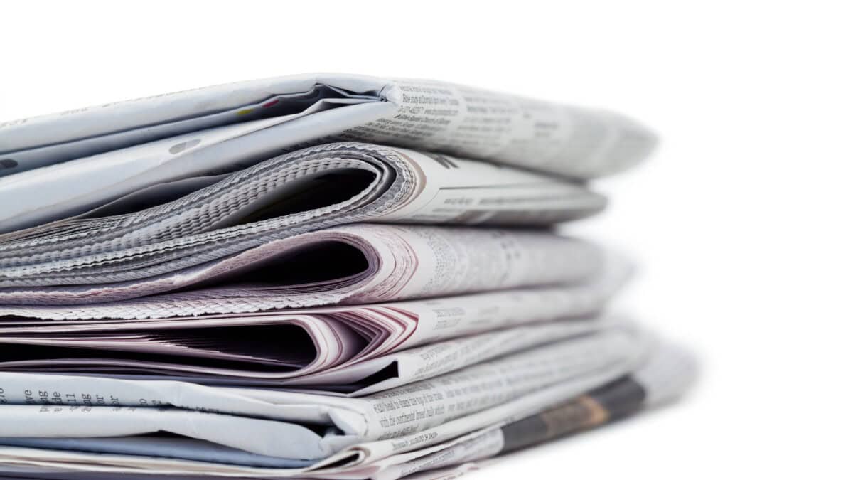 A close-up of a stack of folded newspapers placed on a white surface, with the text on the pages partially visible.